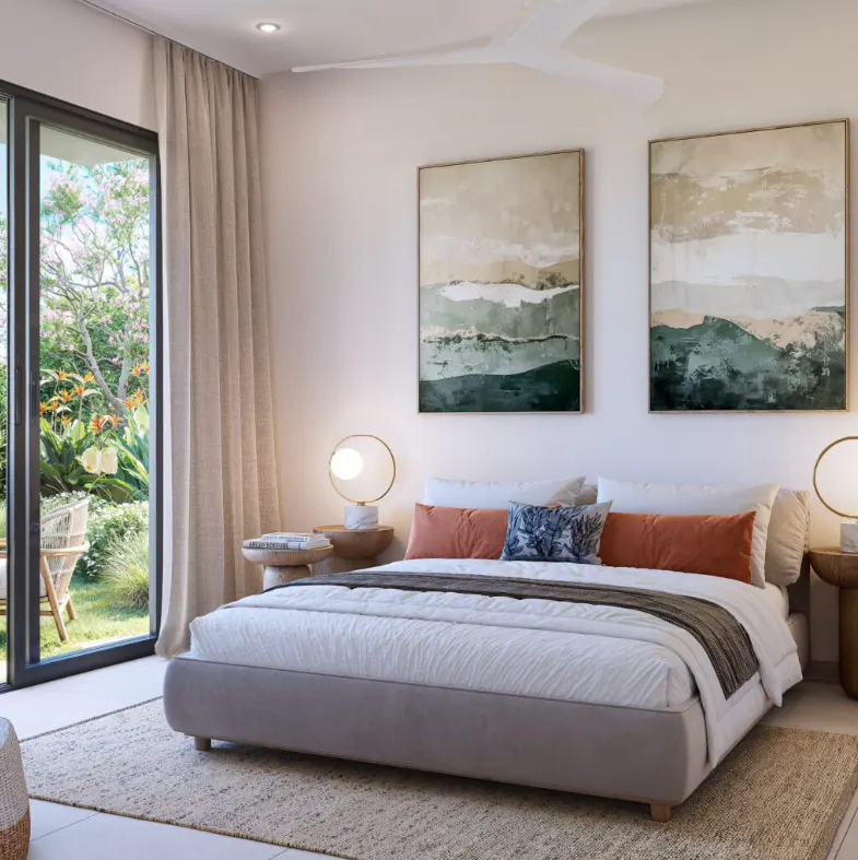 A bright bedroom with a gray bed, white linens, and landscape art. A sliding glass door leads to a lush green garden.