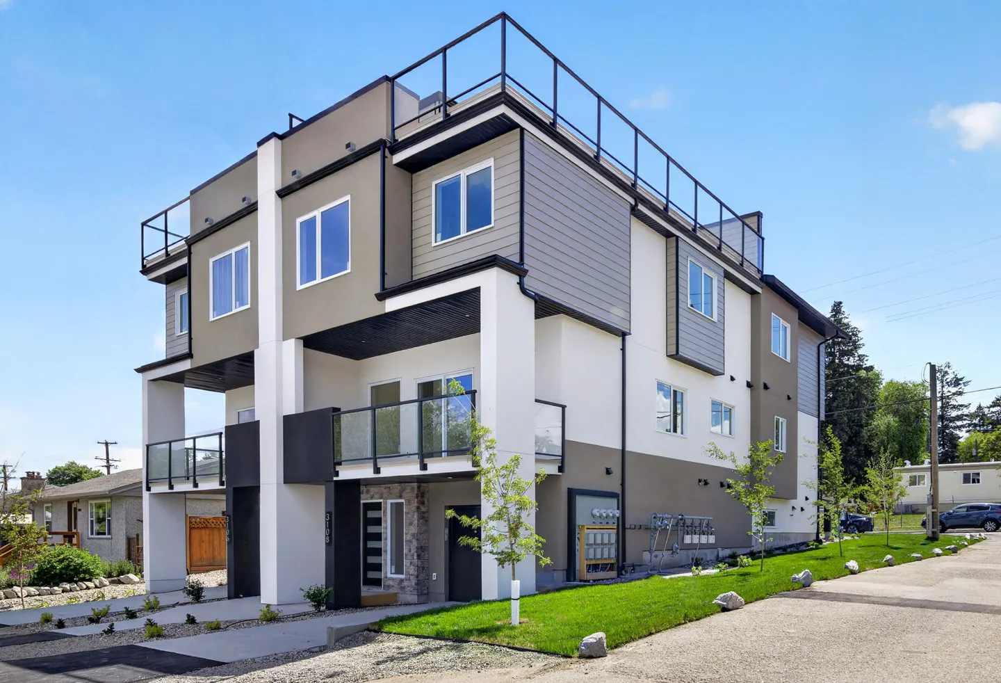 Modern three-story townhouse with a flat roof, rooftop deck, and a mix of white, grey, and tan exterior siding.