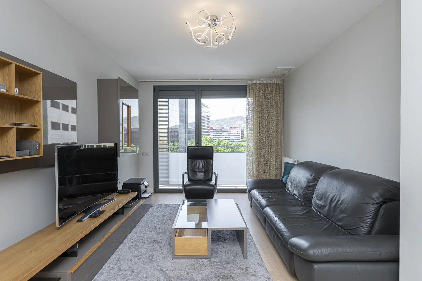 A modern living room with a black leather sofa, chair, and a view of city buildings.