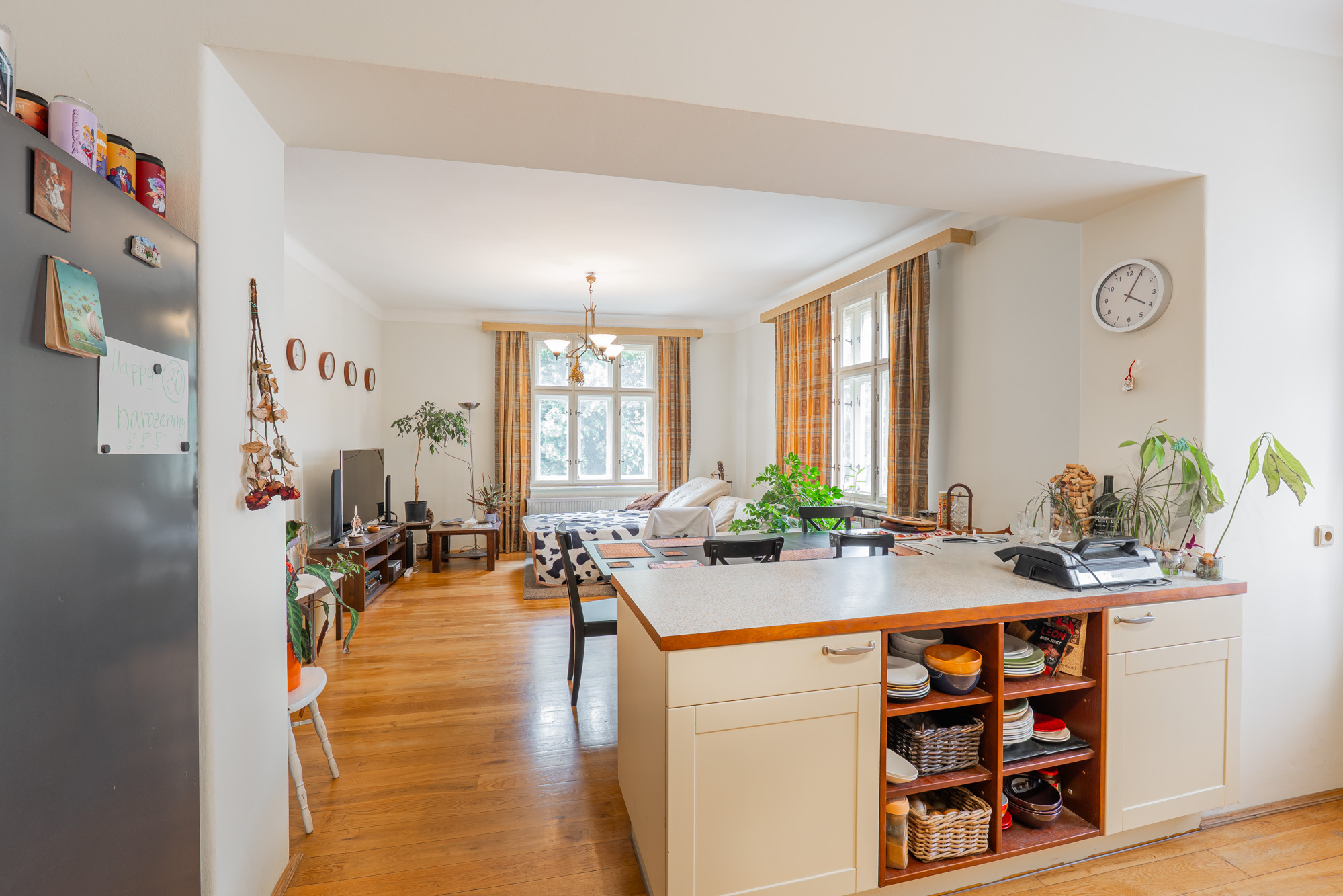 Open-plan kitchen with a white island and shelving, looking into a living room with hardwood floors and large windows.