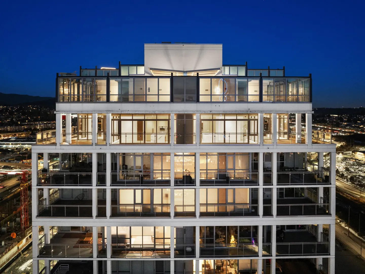 Exterior view of a modern white high-rise apartment building at twilight, featuring glass balconies and illuminated units.