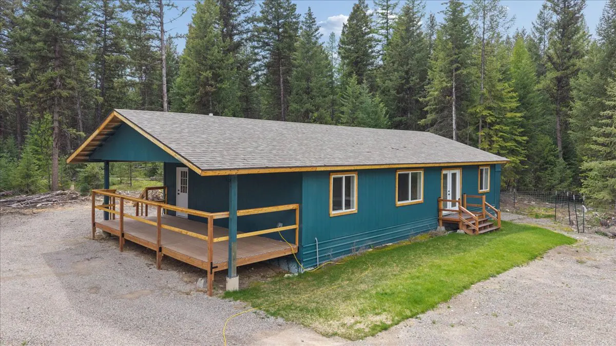 Exterior of a teal house with a gray roof, wooden deck, and forest background.