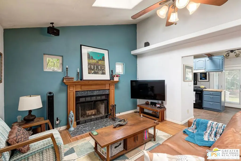 Living room with blue accent wall, fireplace, wood floors, and a brown leather couch. The kitchen is visible in the background.