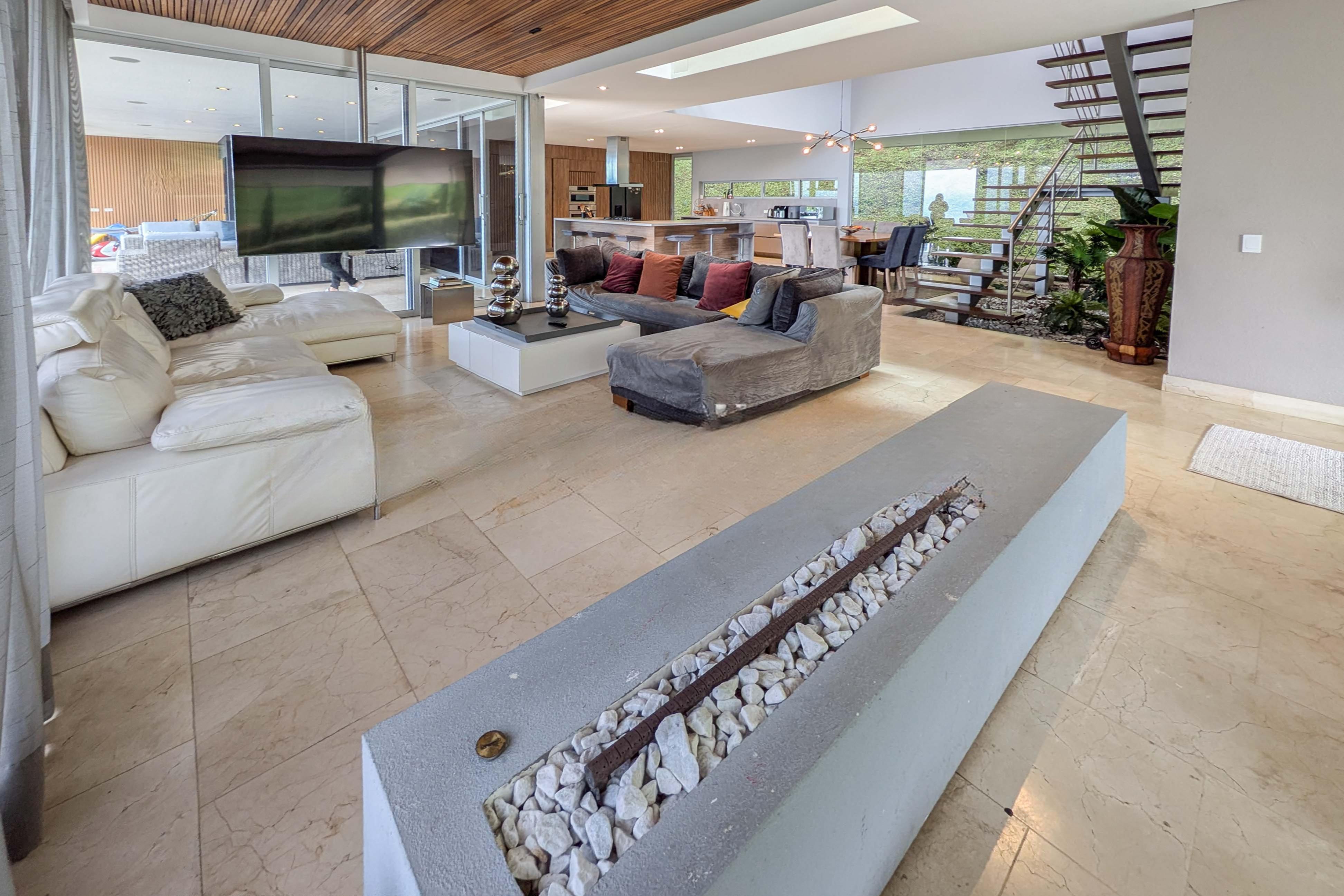 Open-concept living room with white and gray sofas, a modern fireplace, and a view of the kitchen and dining area.