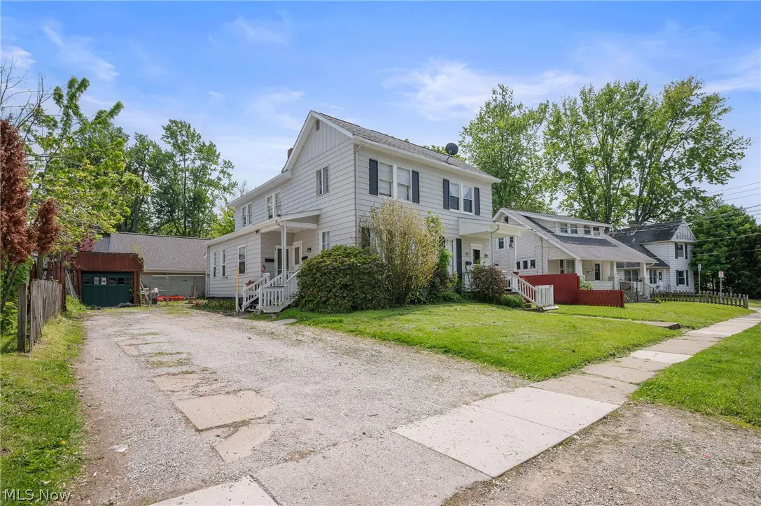 Exterior view of a two-story white duplex with black shutters, a gravel driveway, and green lawn.