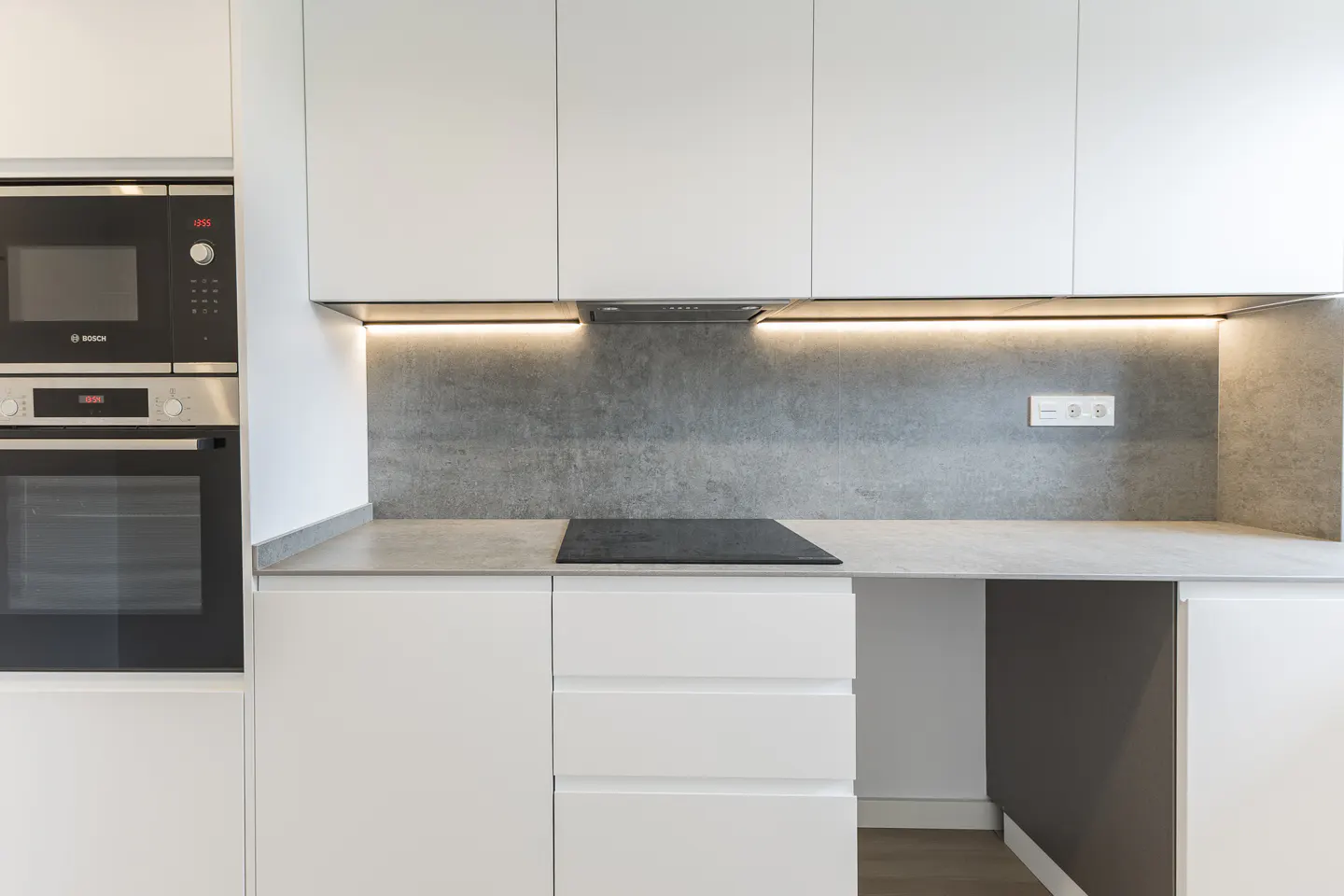 A modern kitchen with white cabinets, a gray backsplash, and a black stovetop. A built-in oven and microwave are on the left.