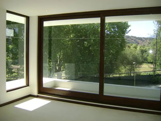 A bright room with large, dark-framed windows showing a green, tree-filled landscape.