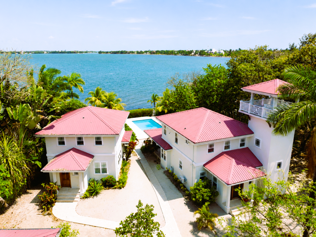 Aerial view of two white houses with red roofs, a pool, and a lighthouse tower by the water.