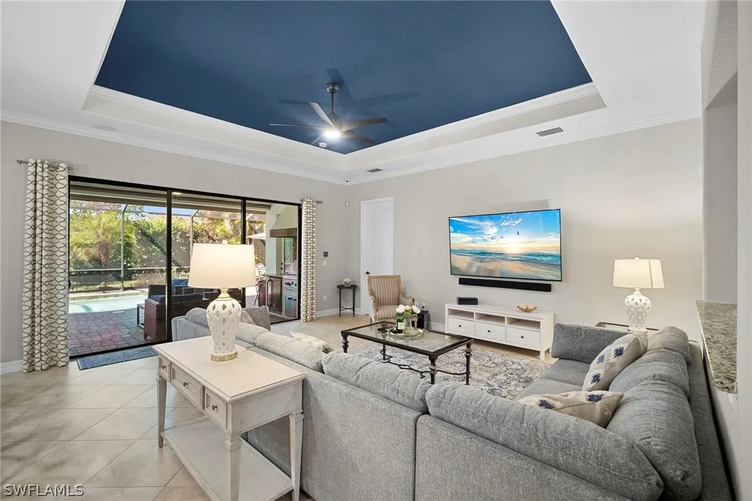 Living room with gray sectional sofa, TV, and sliding glass doors to a pool area. The ceiling has a blue inset.