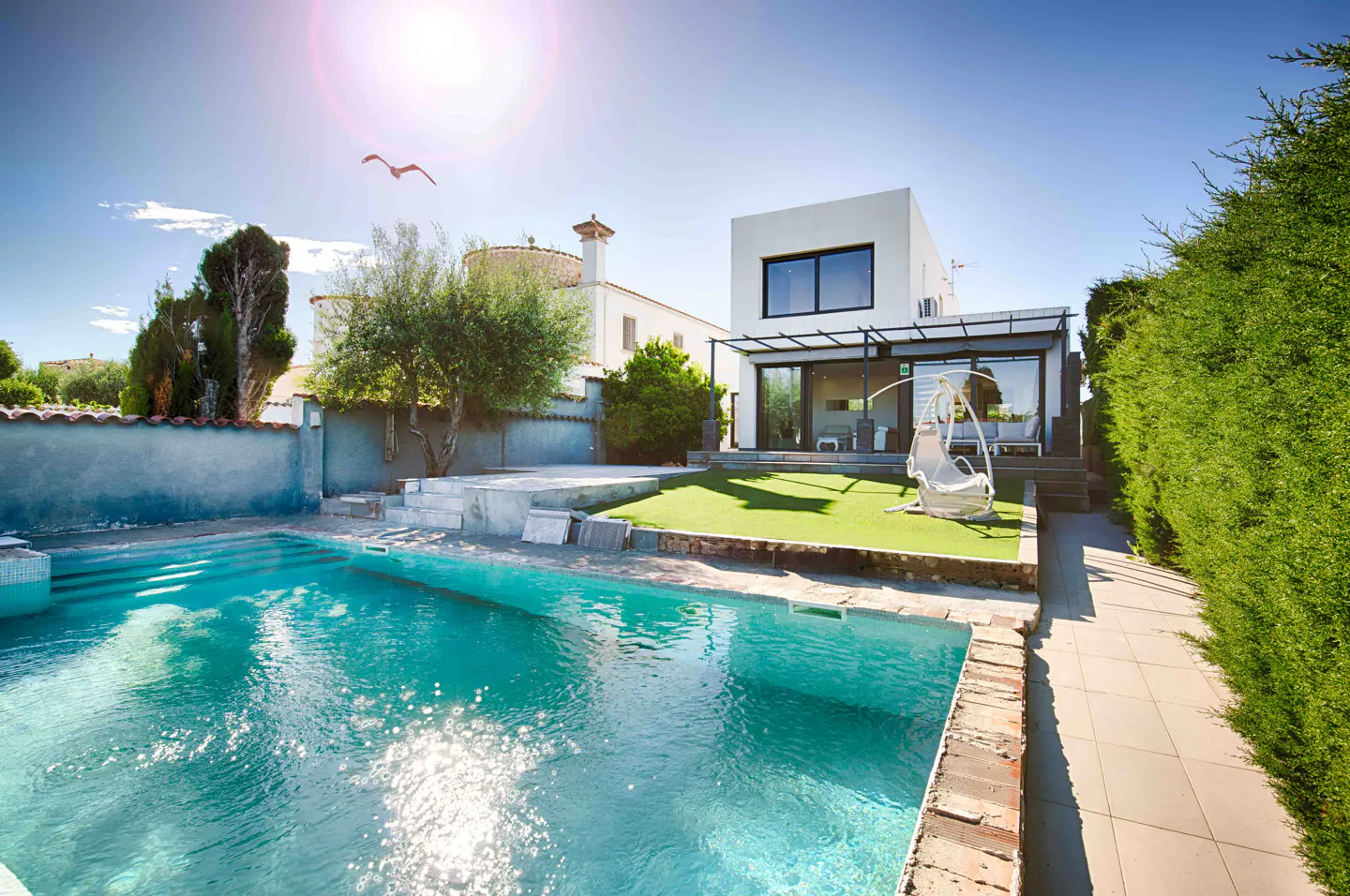 A modern white house with a pool and a hanging chair on a sunny day.
