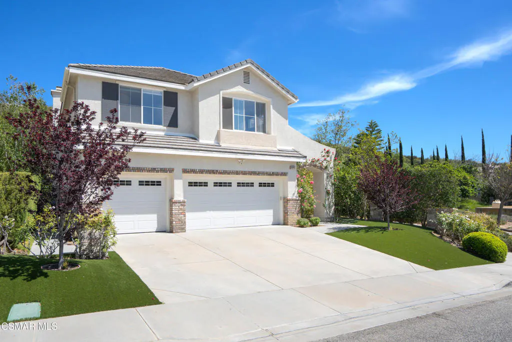 Two-story house with a two-car garage, white exterior, gray shutters, and a concrete driveway under a blue sky.