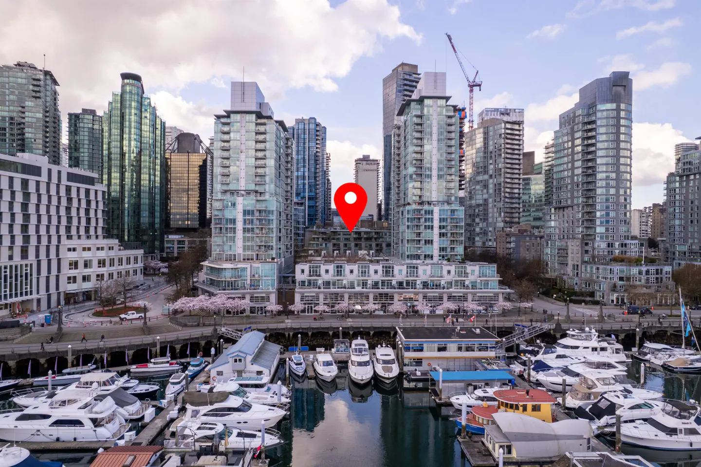 Aerial view of a city marina with boats, tall buildings, and a red location pin.