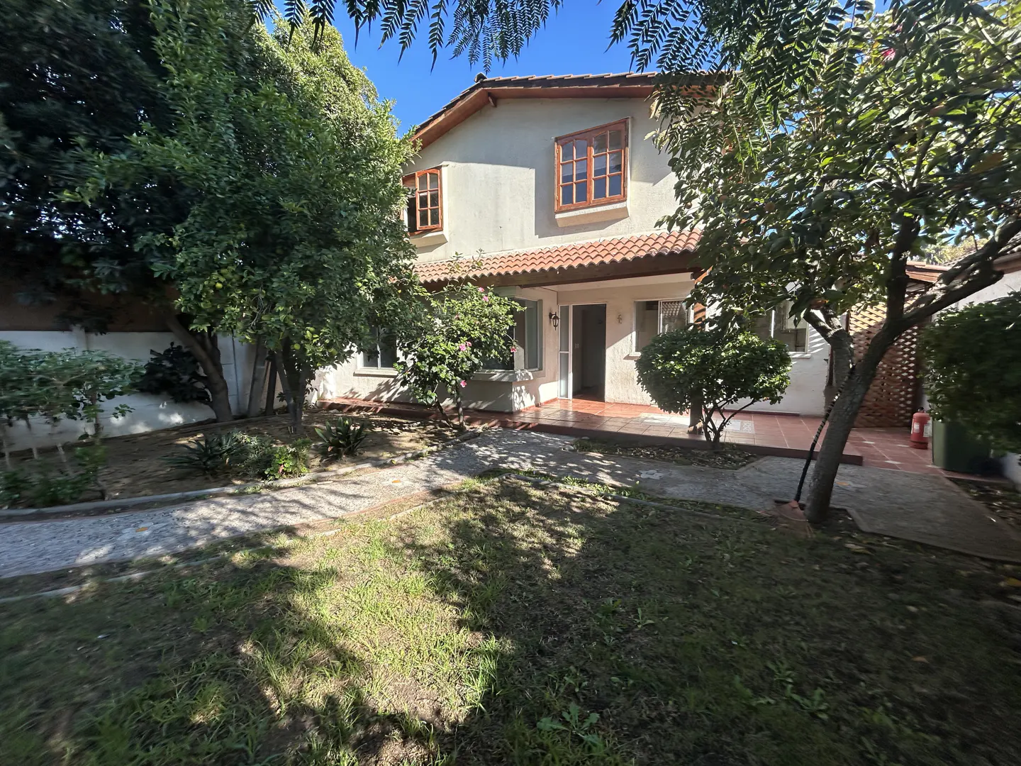 Two-story house with a red tile roof and a lawn with trees in the front yard.
