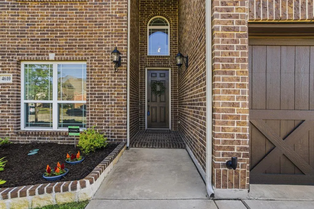 Exterior shot of a brick house with a brown front door, a wreath, and a brown garage door. There is a flower bed with red flowers.