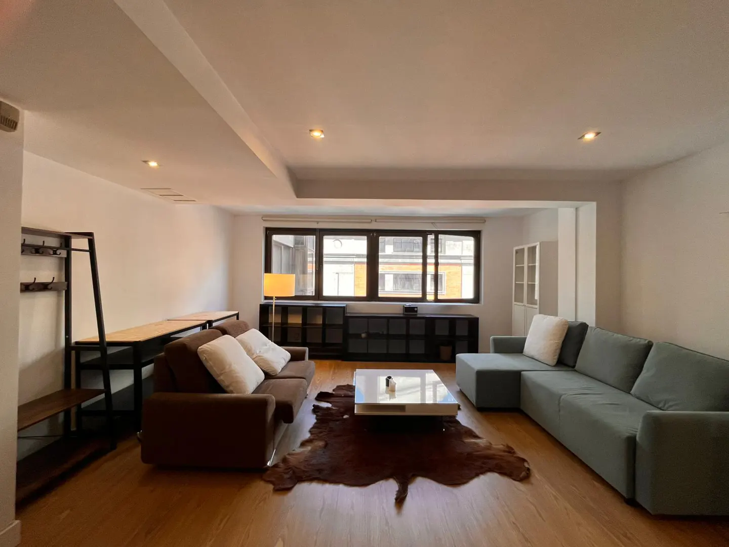 Spacious living room with a brown sofa, grey sectional, white coffee table, and cowhide rug on light wood floors.