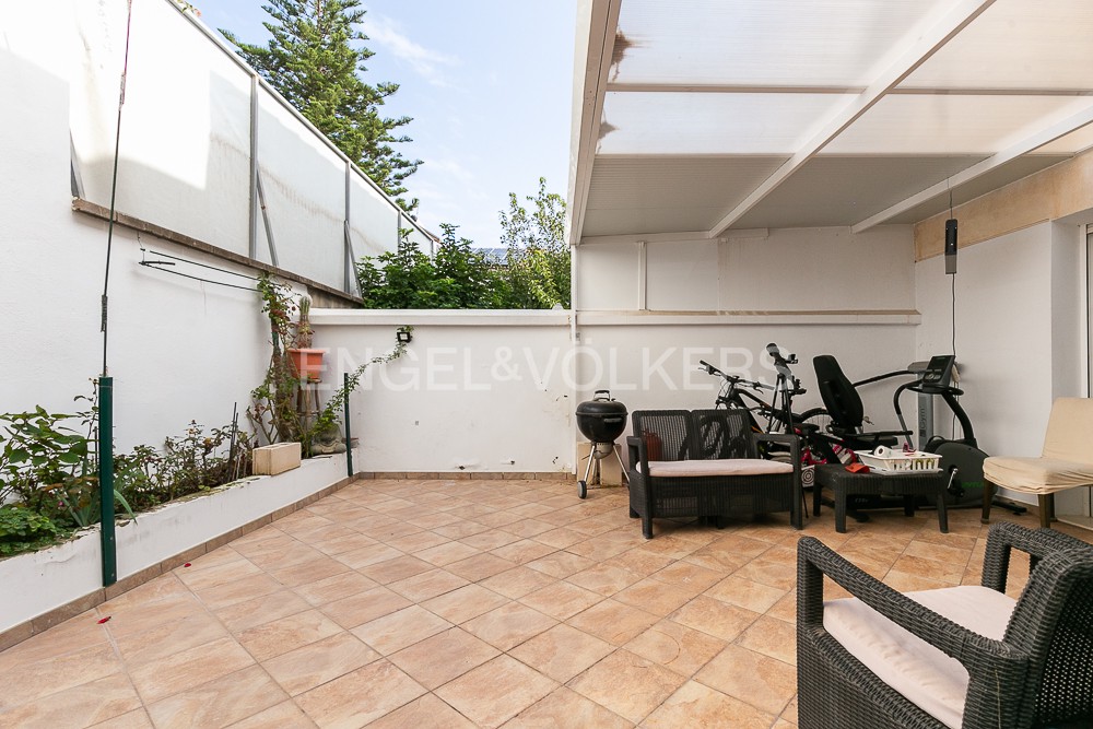 A tiled outdoor patio with a covered area, featuring a grill, exercise equipment, and wicker furniture against white walls. [AI-generated text]