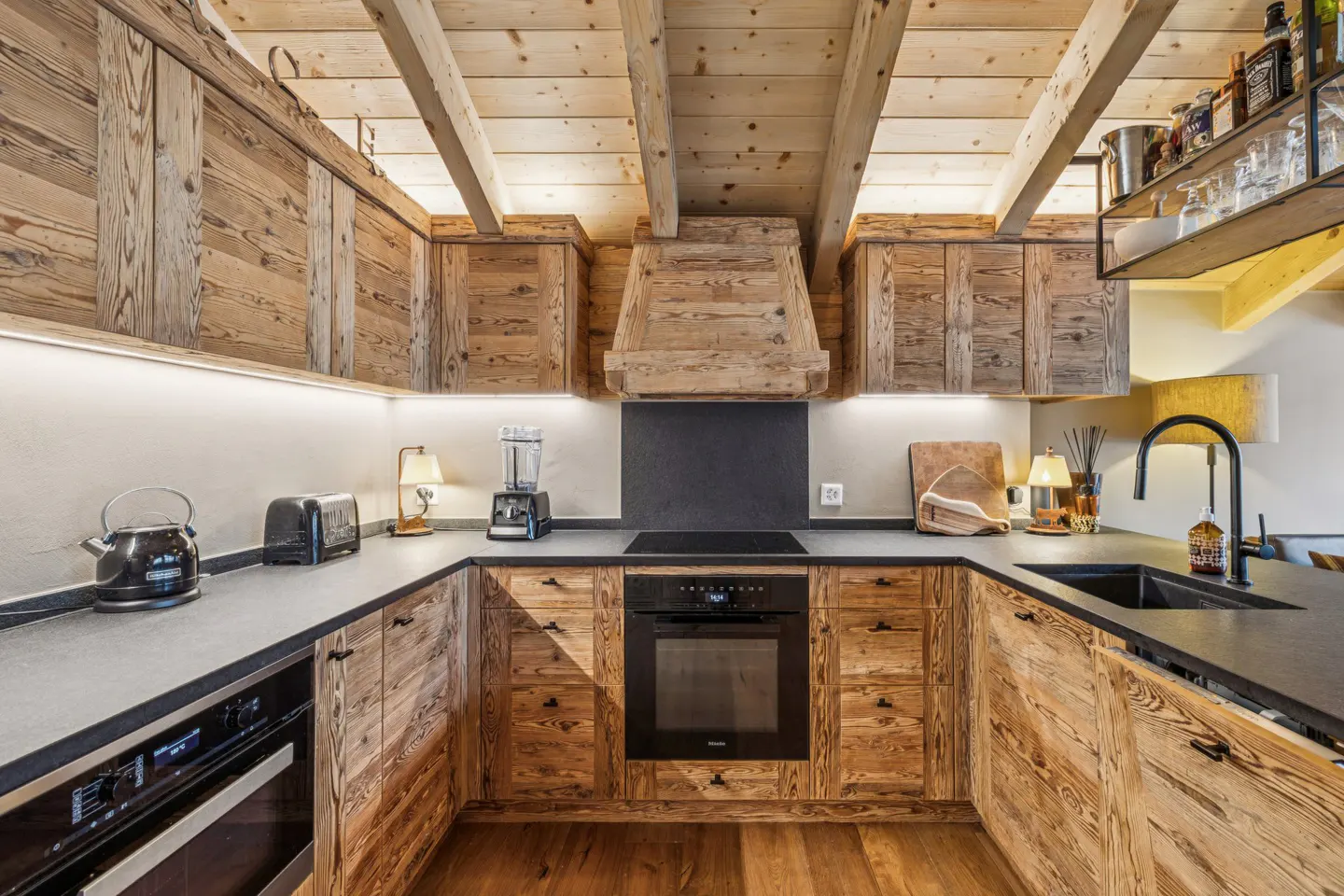 Rustic kitchen with wood cabinets, black countertops, and stainless steel appliances. Wood ceiling with exposed beams.