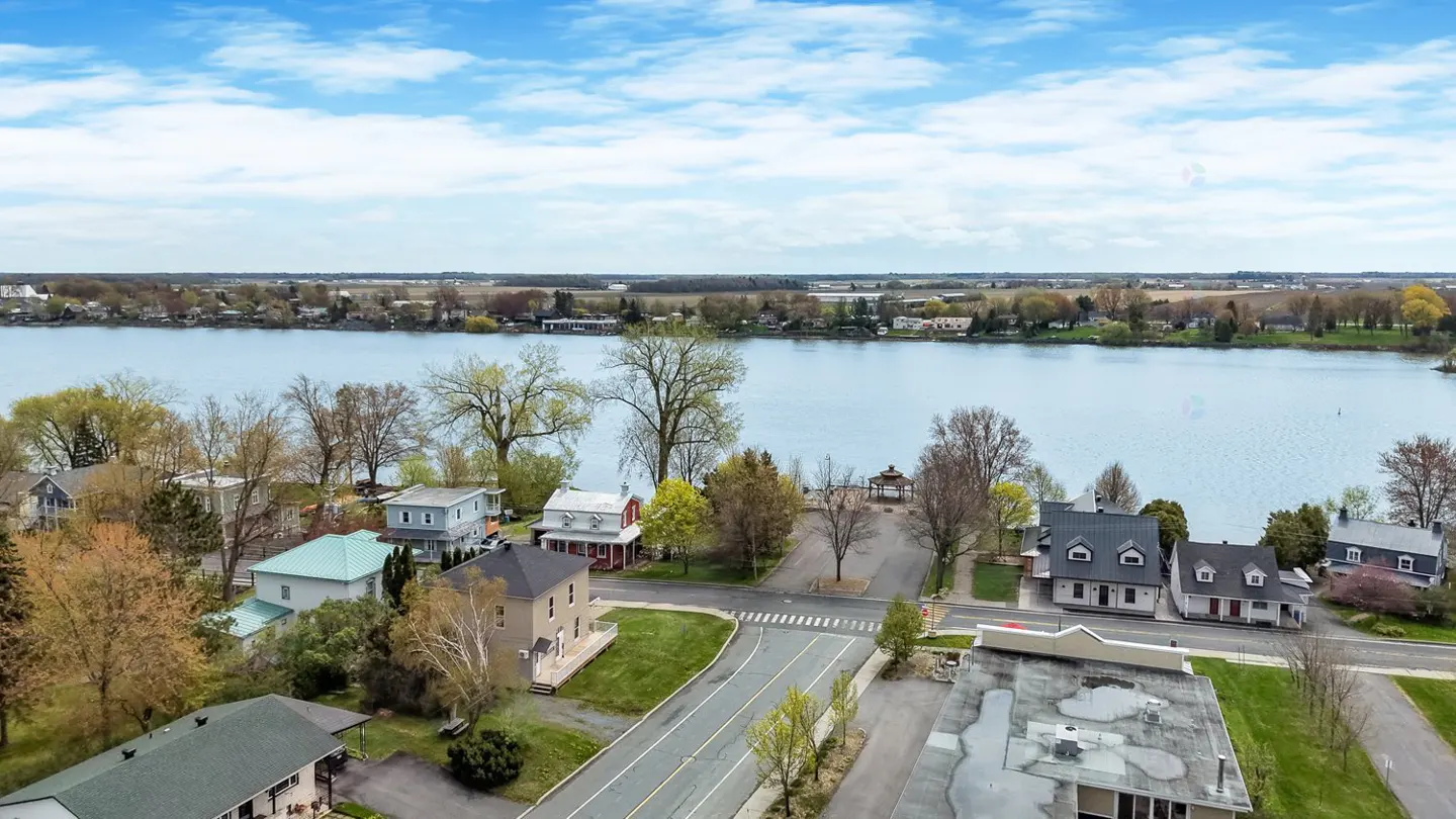 Aerial view of waterfront homes on a sunny day. A lake is in the background with a blue sky and white clouds.