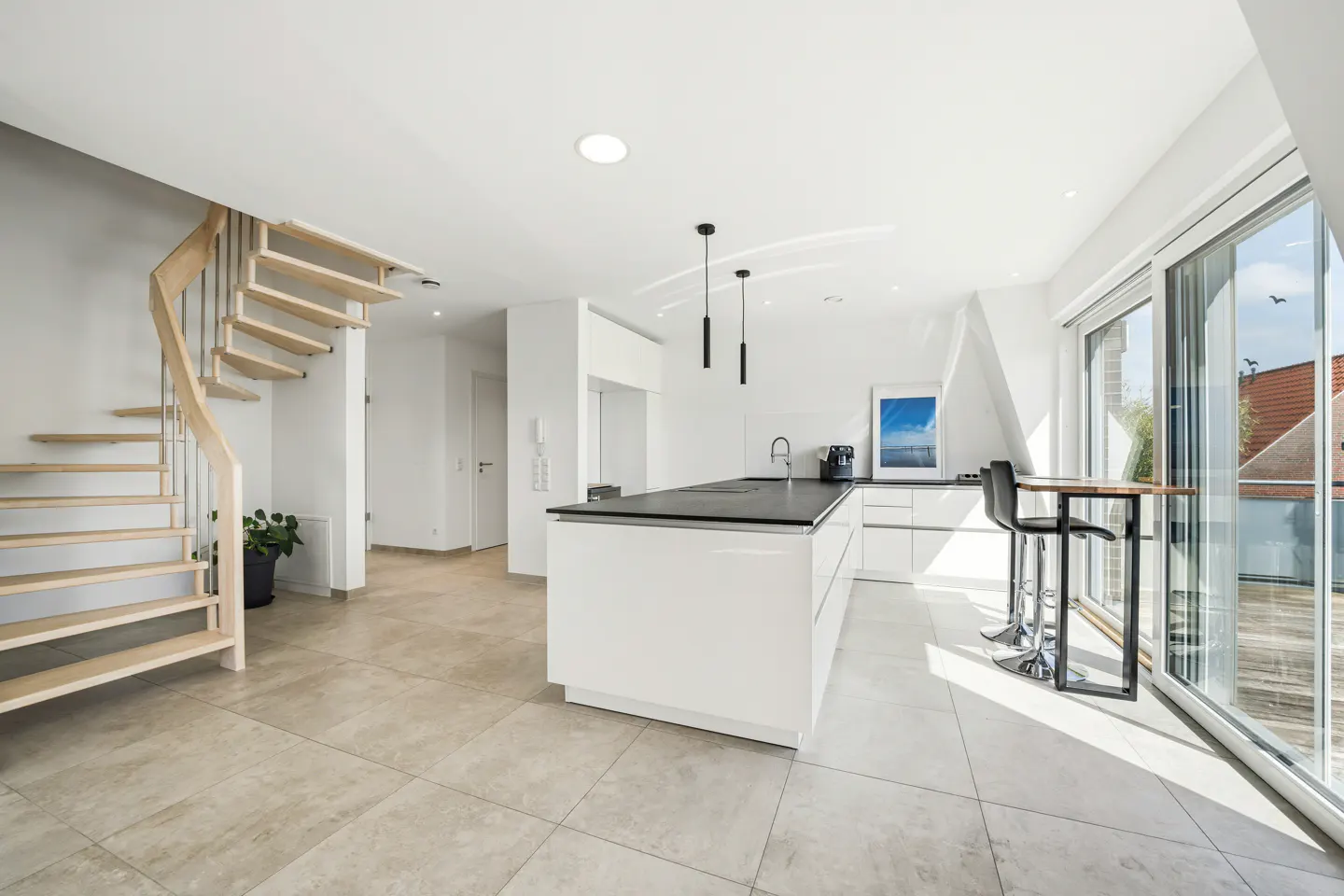 Bright, modern kitchen with white cabinets, black countertops, and a wooden spiral staircase. Large sliding glass doors lead to a balcony.