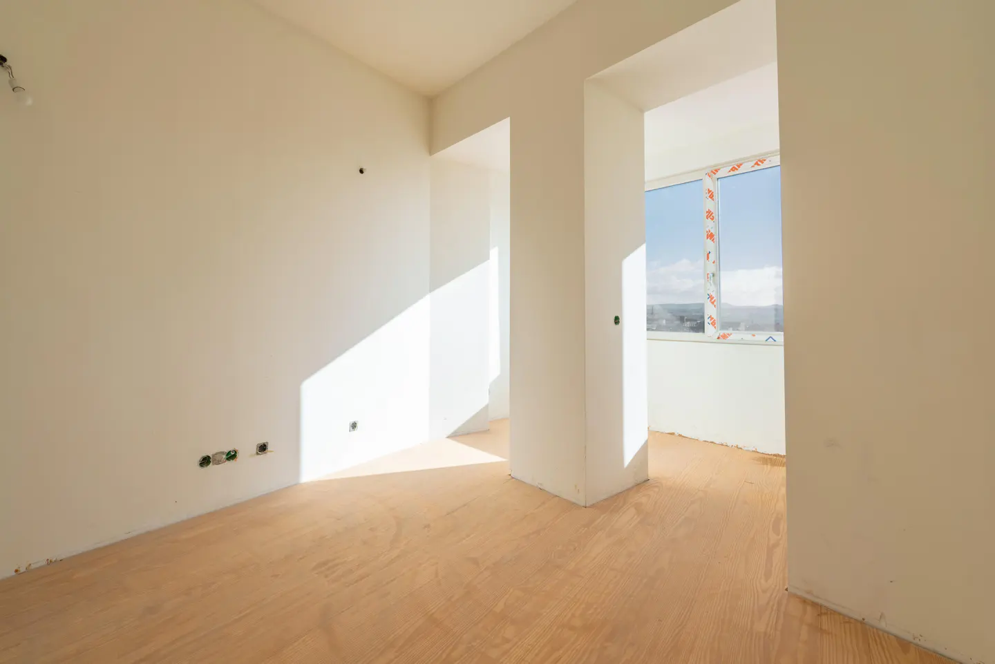 Unfinished room with light wood floors, white walls, and a window with a view. Sunlight streams in.