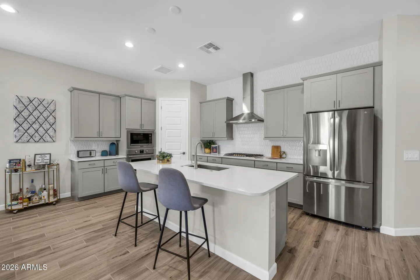 Bright kitchen with gray cabinets, stainless steel appliances, and a white countertop island with two blue chairs.