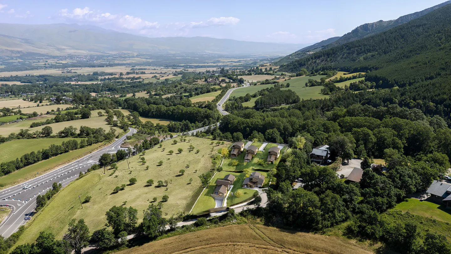Aerial view of modern homes on a green hillside, with mountains and a valley in the background.