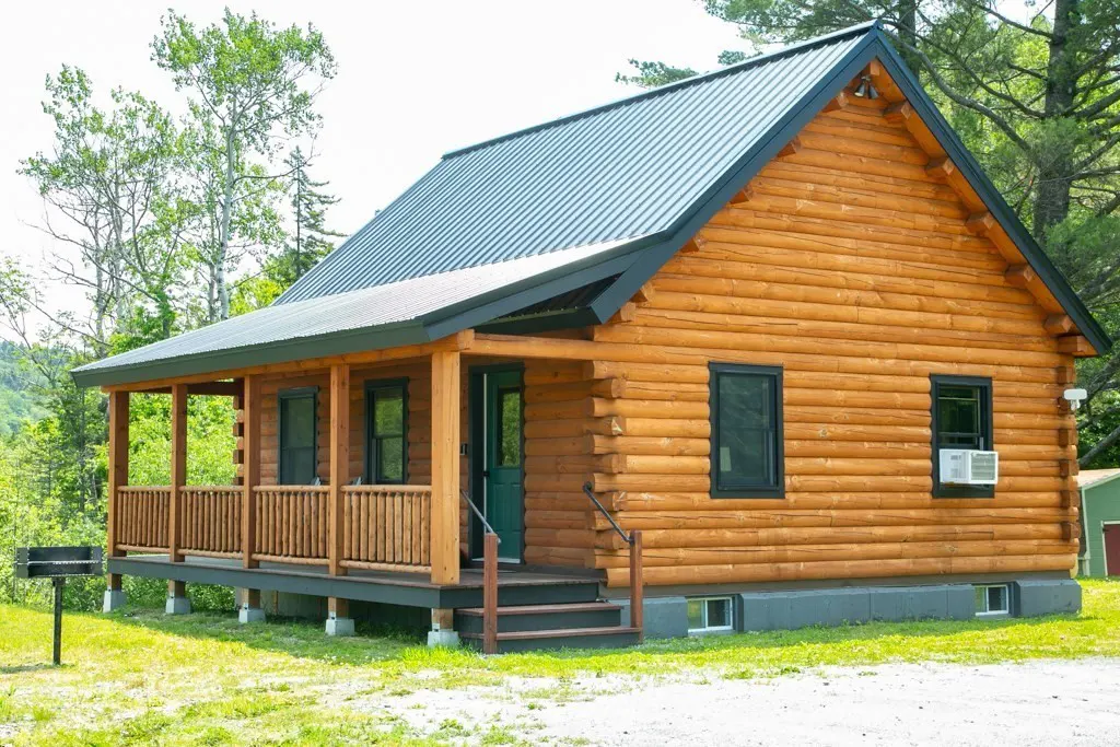 Exterior view of a log cabin with a metal roof, a porch, and a green door.