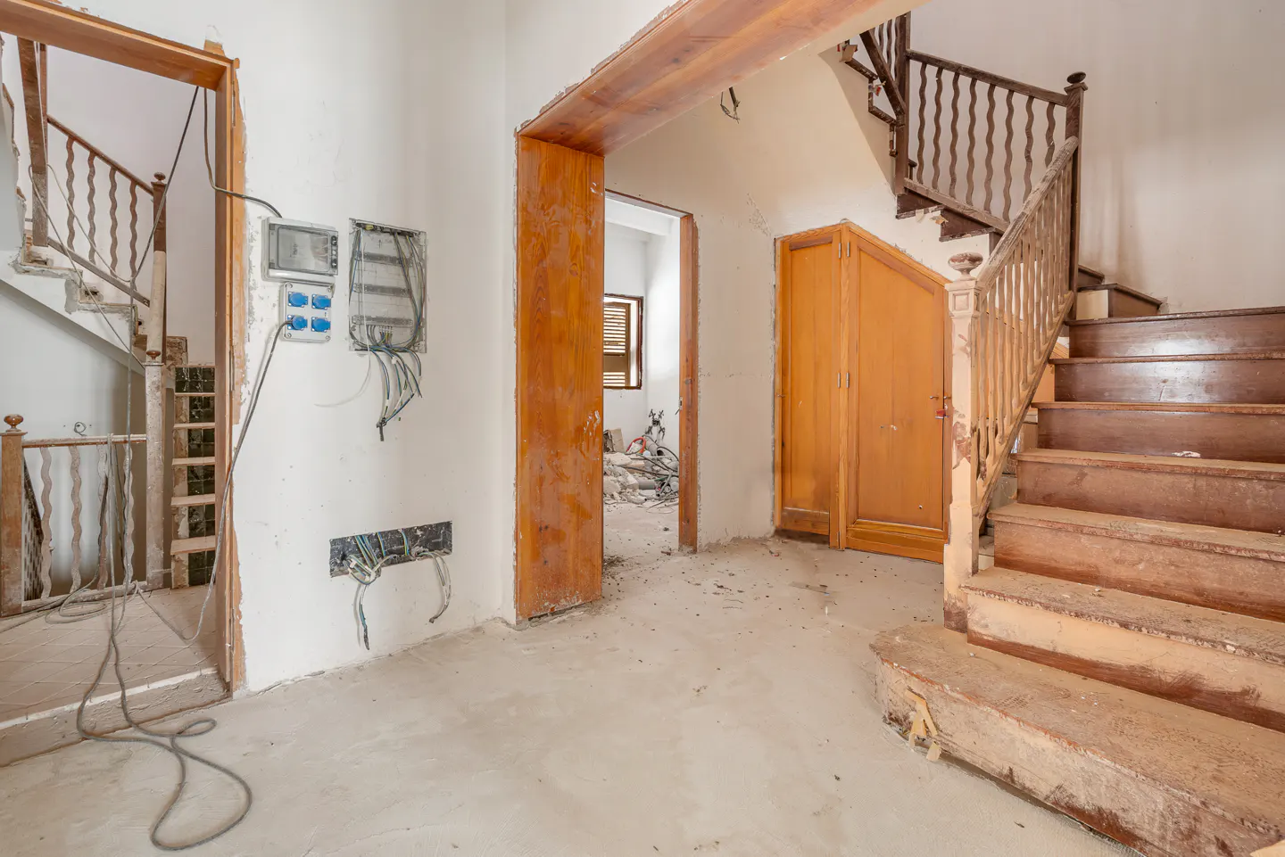 Interior view of a home under renovation, featuring wooden stairs, exposed wiring, and unfinished walls.