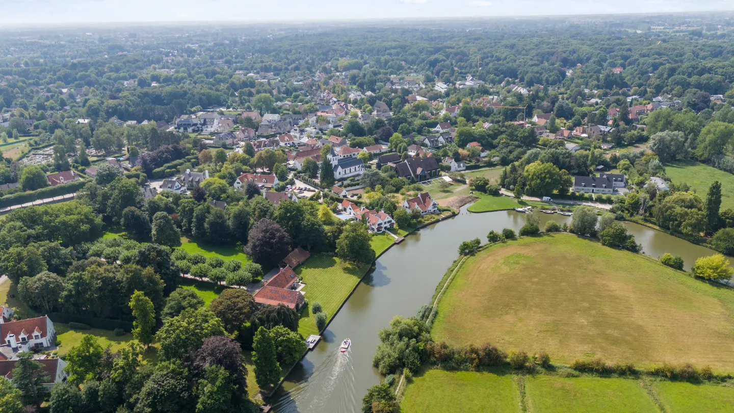 Aerial view of a village with houses, trees, a river, and a boat on the water.