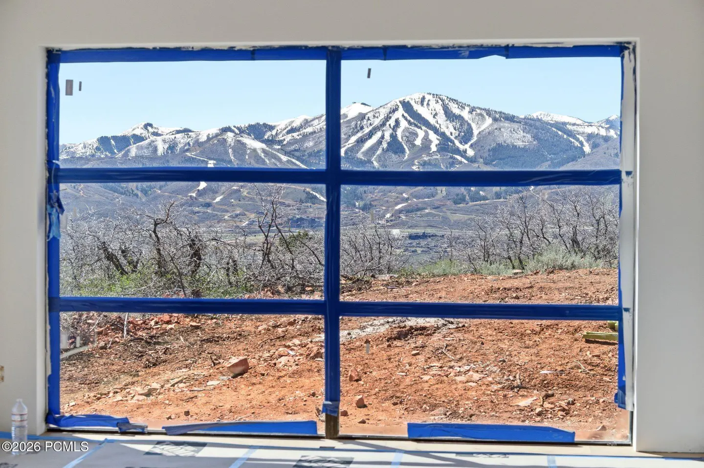 View from a window taped with blue tape, showing a mountain range with ski slopes in the background.