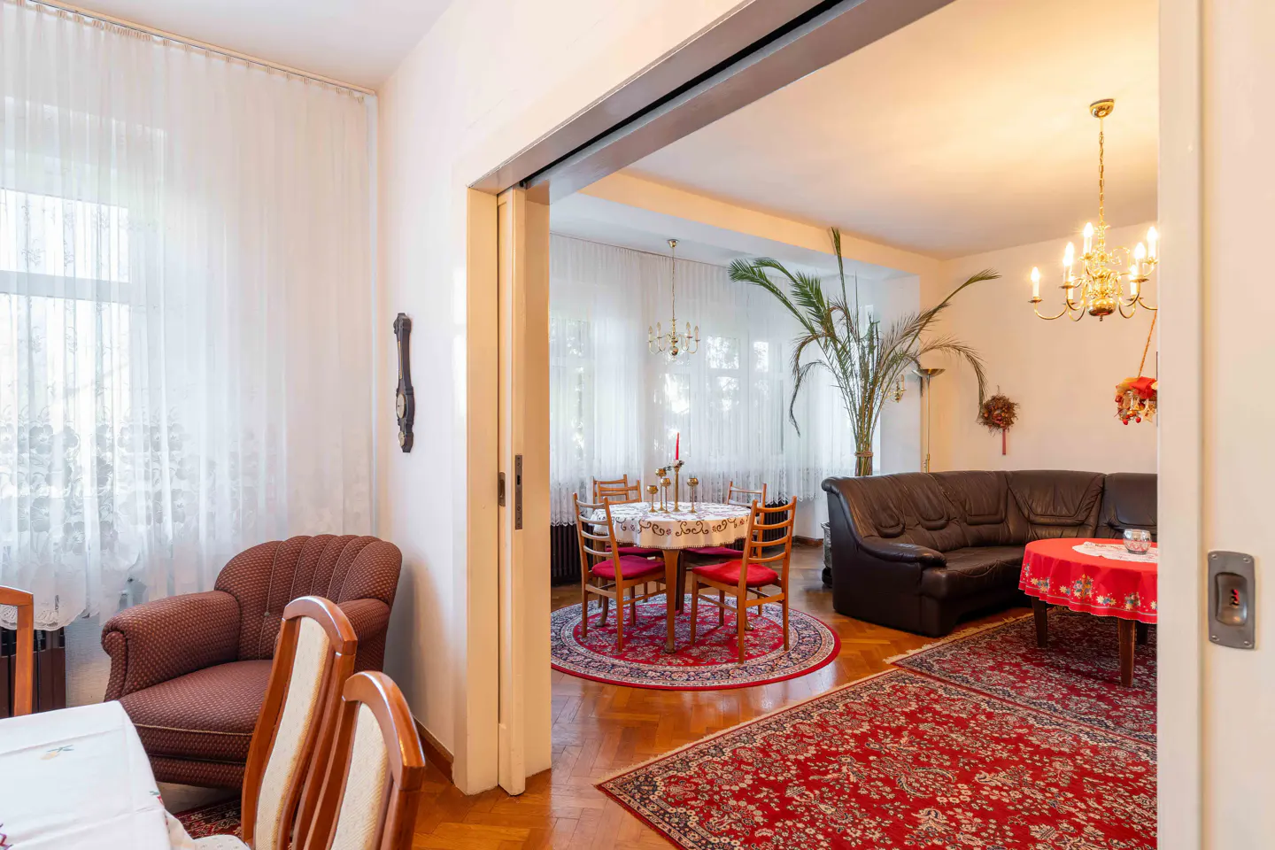A view through a doorway into a living room with a dining table, brown leather sofa, and red rugs.