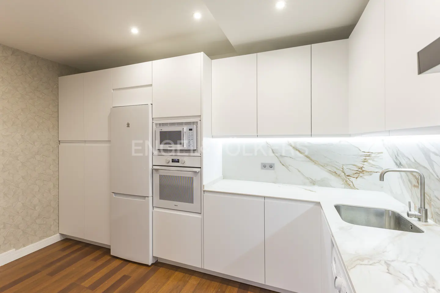 Bright, modern kitchen with white cabinets, marble countertops, stainless steel sink and appliances, and wood floors.