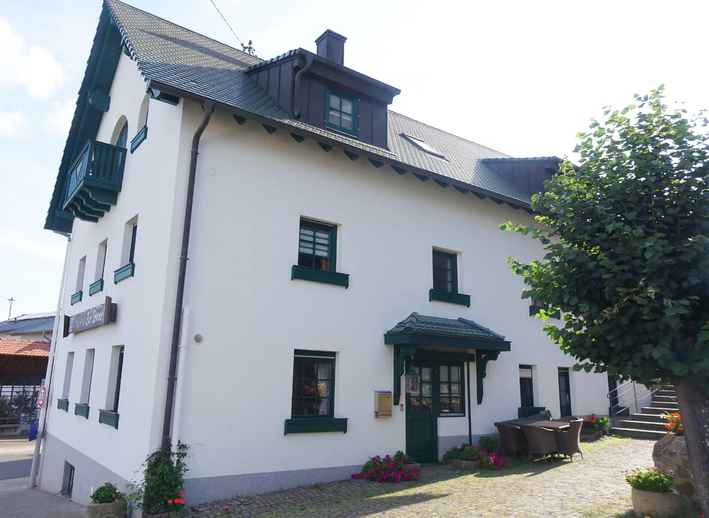 A two-story white building with green trim and a dark gray roof. A tree is on the right side of the building.