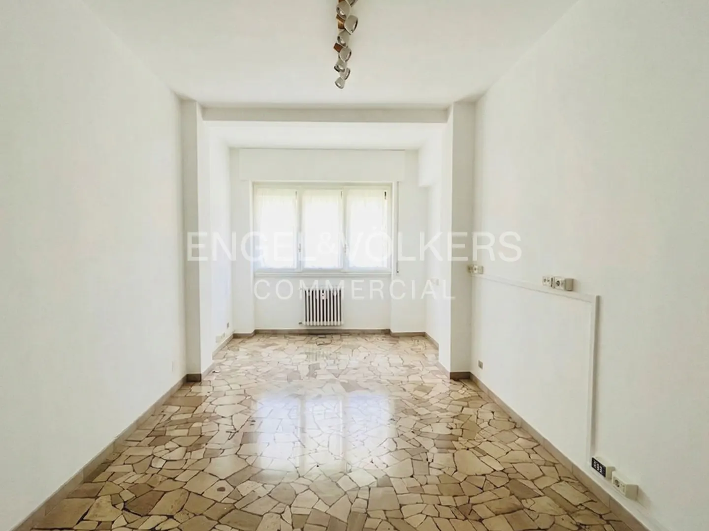 Empty white room with mosaic tile floor, radiator under window, and modern ceiling light fixture.