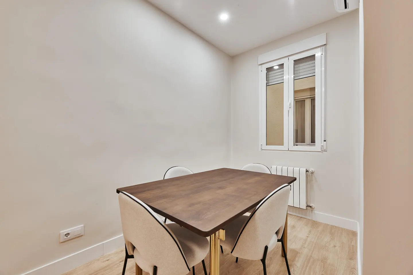 A dining room with a dark wood table, four cream chairs, and a white window.