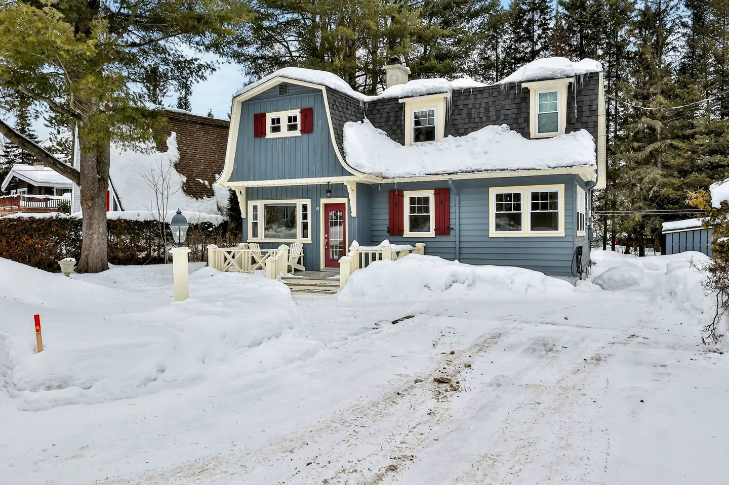 A blue house with red shutters and a black roof is covered in snow.