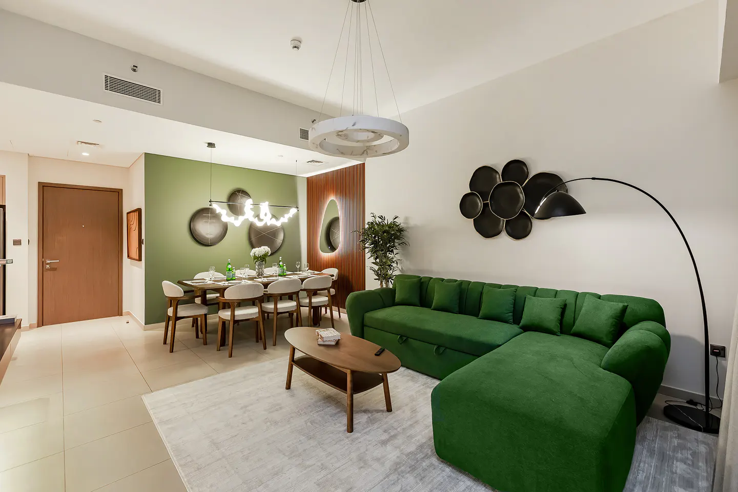 A modern living and dining area with a green velvet sofa, dining table, and decorative lighting.