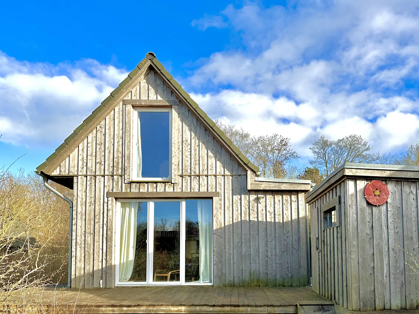 Exterior view of a light gray, wood-sided house with a gabled roof and a blue sky with white clouds in the background.