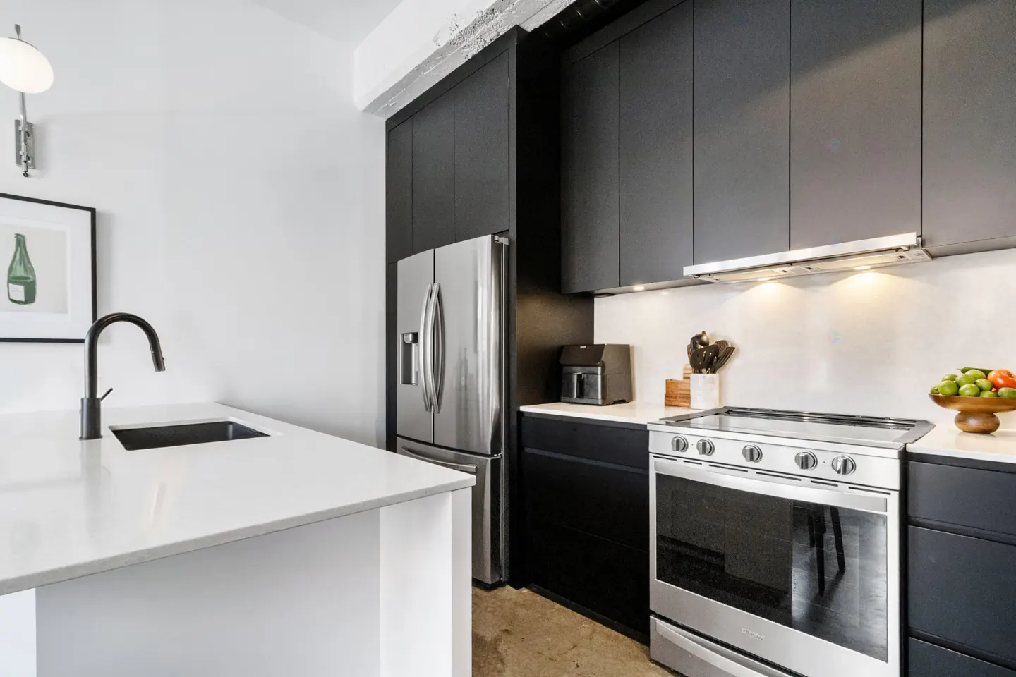 A modern kitchen with black cabinets, stainless steel appliances, and a white countertop island.