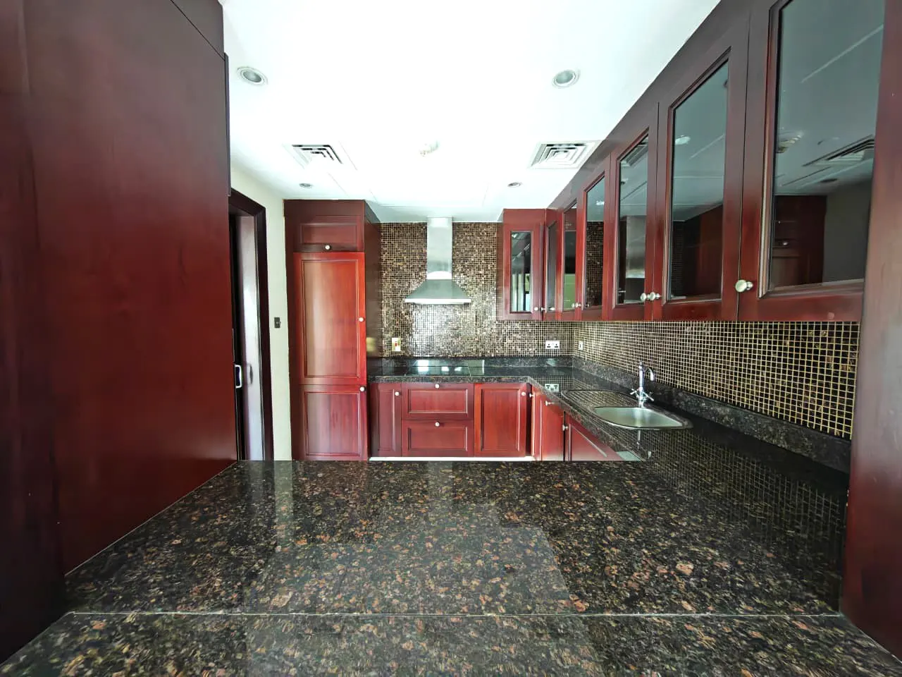 A kitchen with dark brown cabinets, granite countertops, and a mosaic tile backsplash. A stainless steel range hood is centered above the stove.