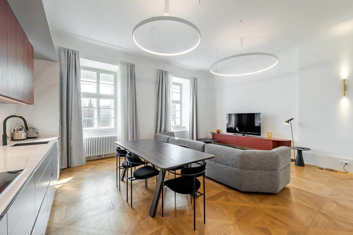 Modern open-plan living area with a grey sofa, dining table, kitchen counter, and two large circular pendant lights.