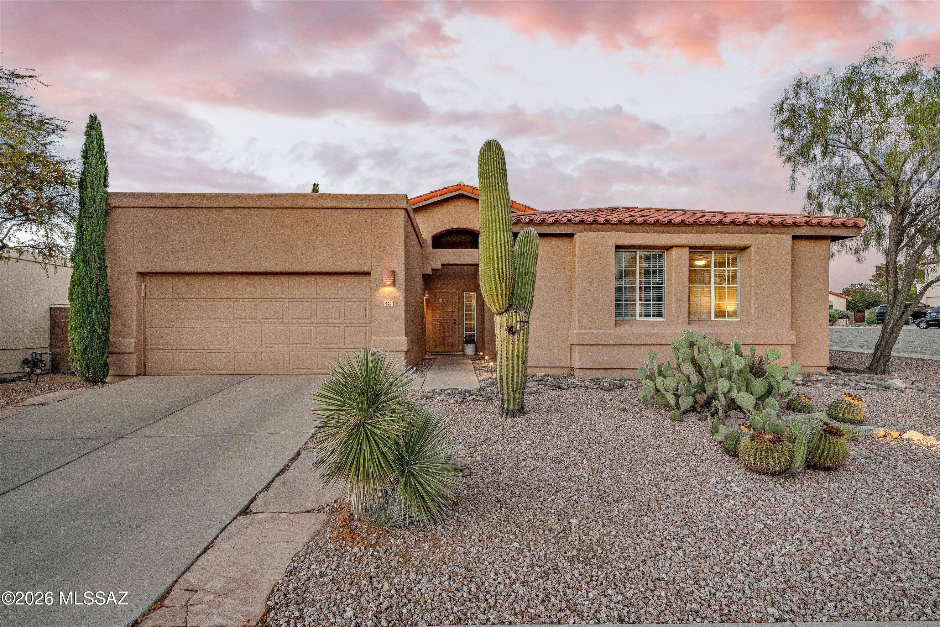 Tan stucco home with a red tile roof, desert landscaping, and a pink and purple sunset sky.