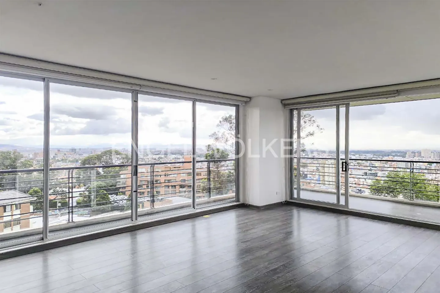 Empty room with dark wood floors and large sliding glass doors leading to balconies with city views.