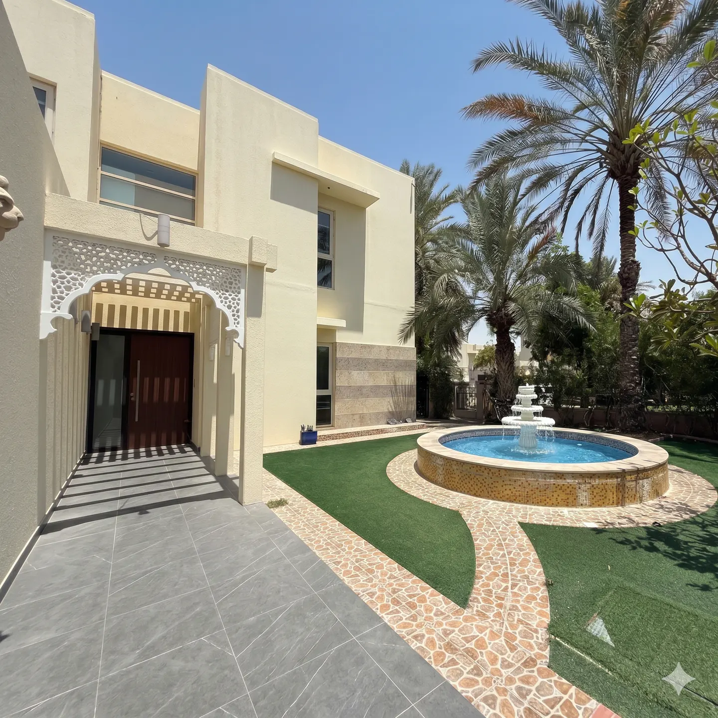 Exterior view of a two-story beige house with a fountain, palm trees, and a gray tiled walkway.