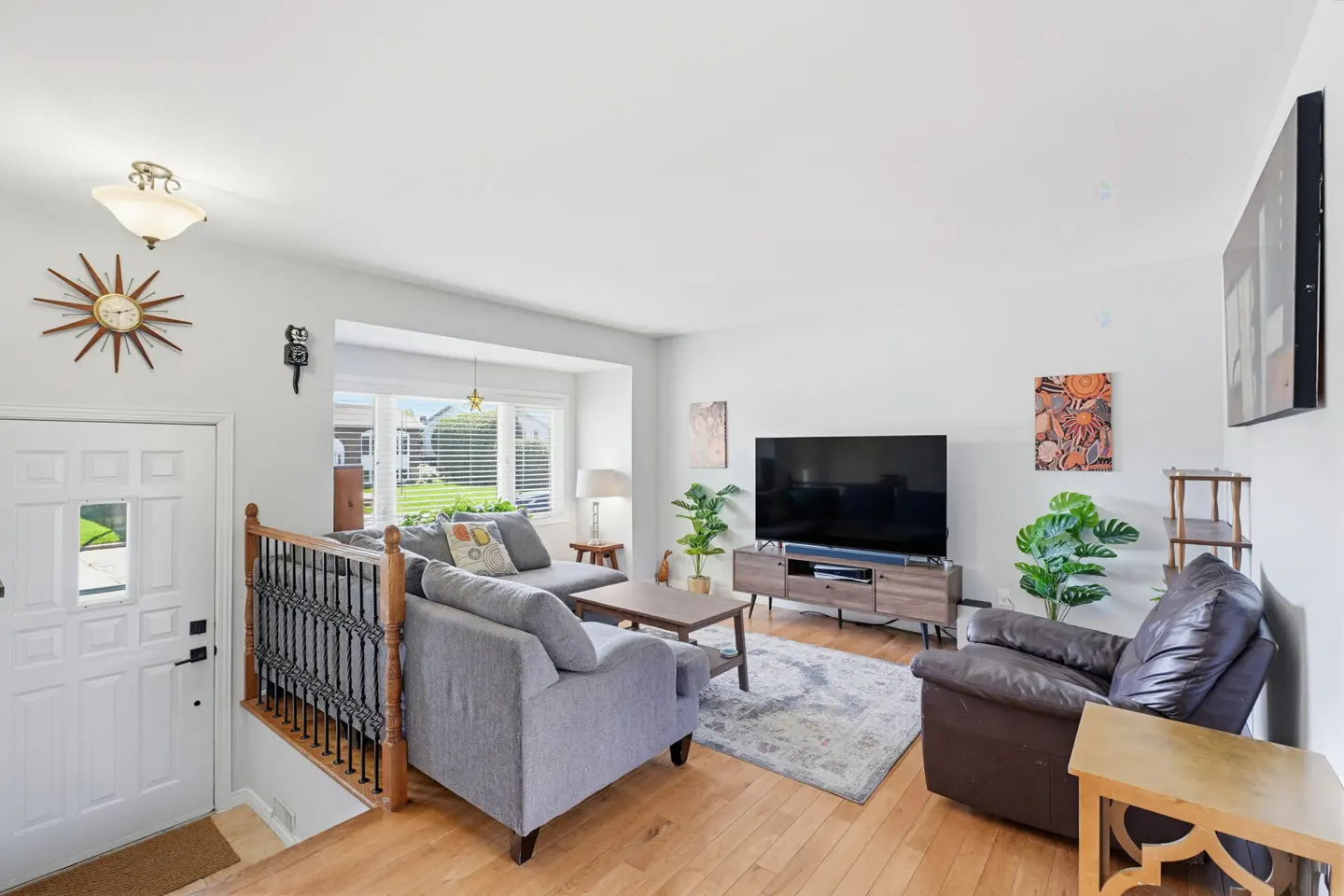 Bright living room with hardwood floors, a gray sectional sofa, a dark leather recliner, and a large TV on a wood console.