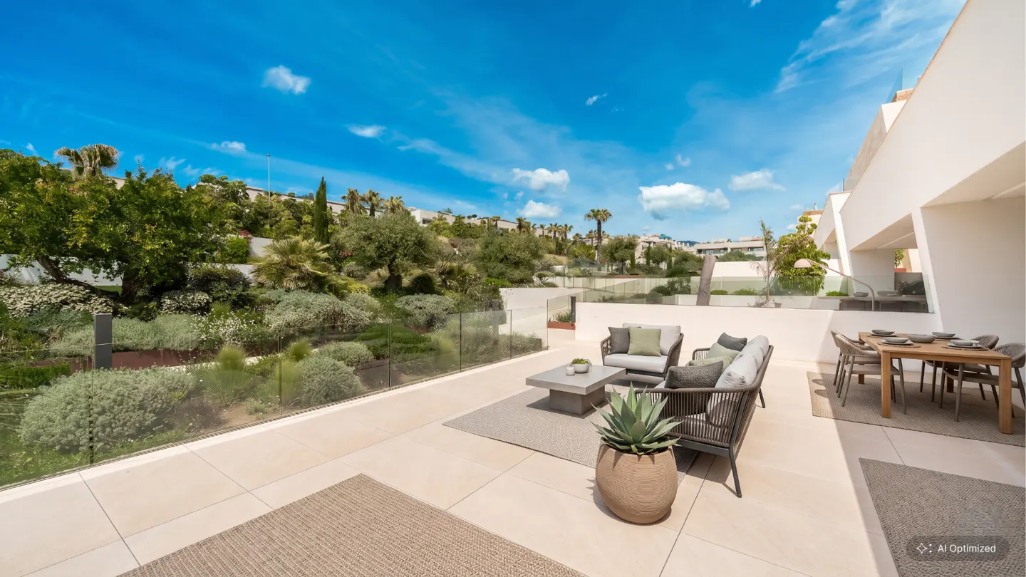 Outdoor patio with dining table, chairs, and lounge seating. Lush green landscape and blue sky in the background.