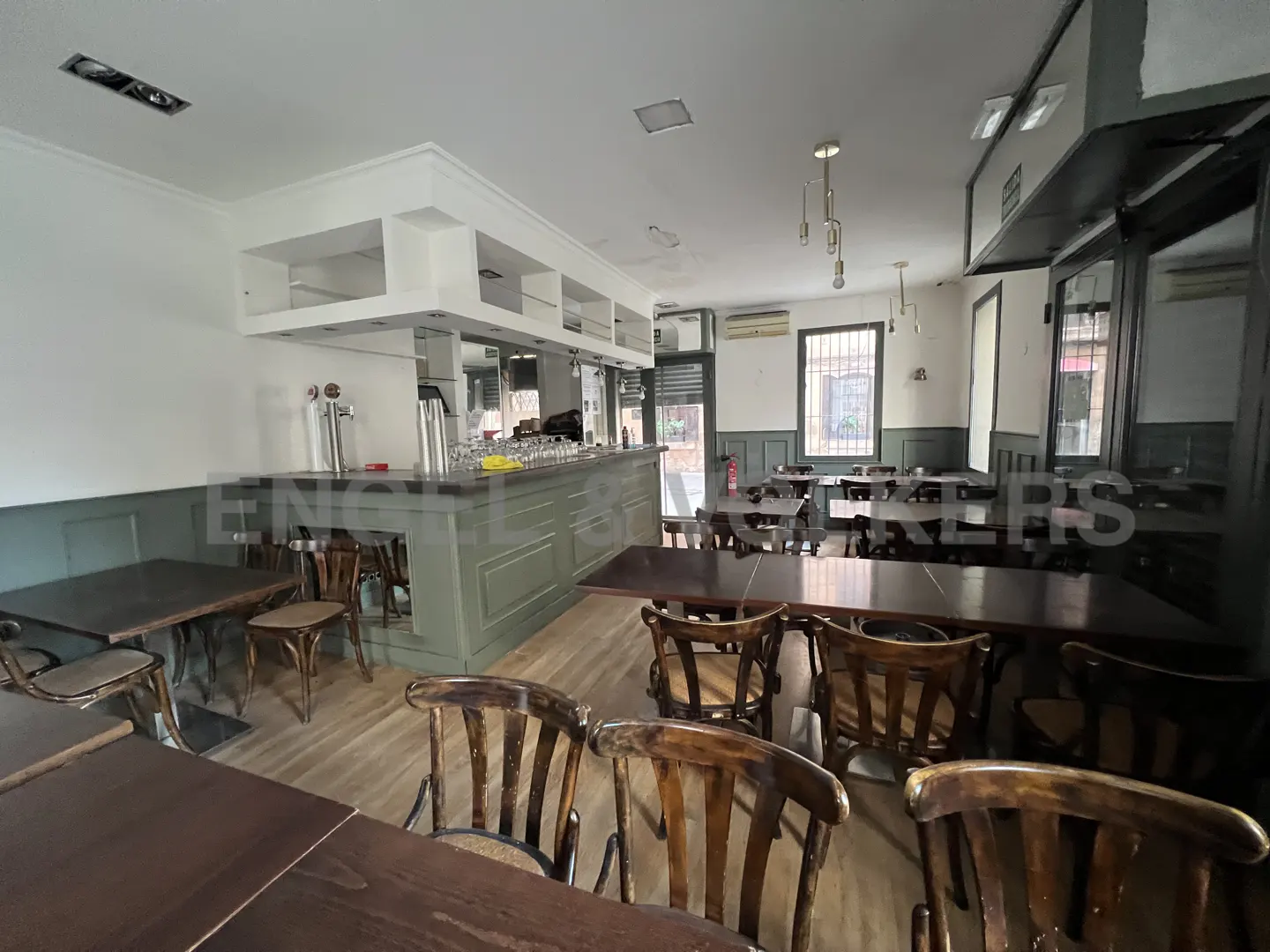 Interior view of a restaurant with wooden tables and chairs, a bar with beer taps, and natural light from windows.