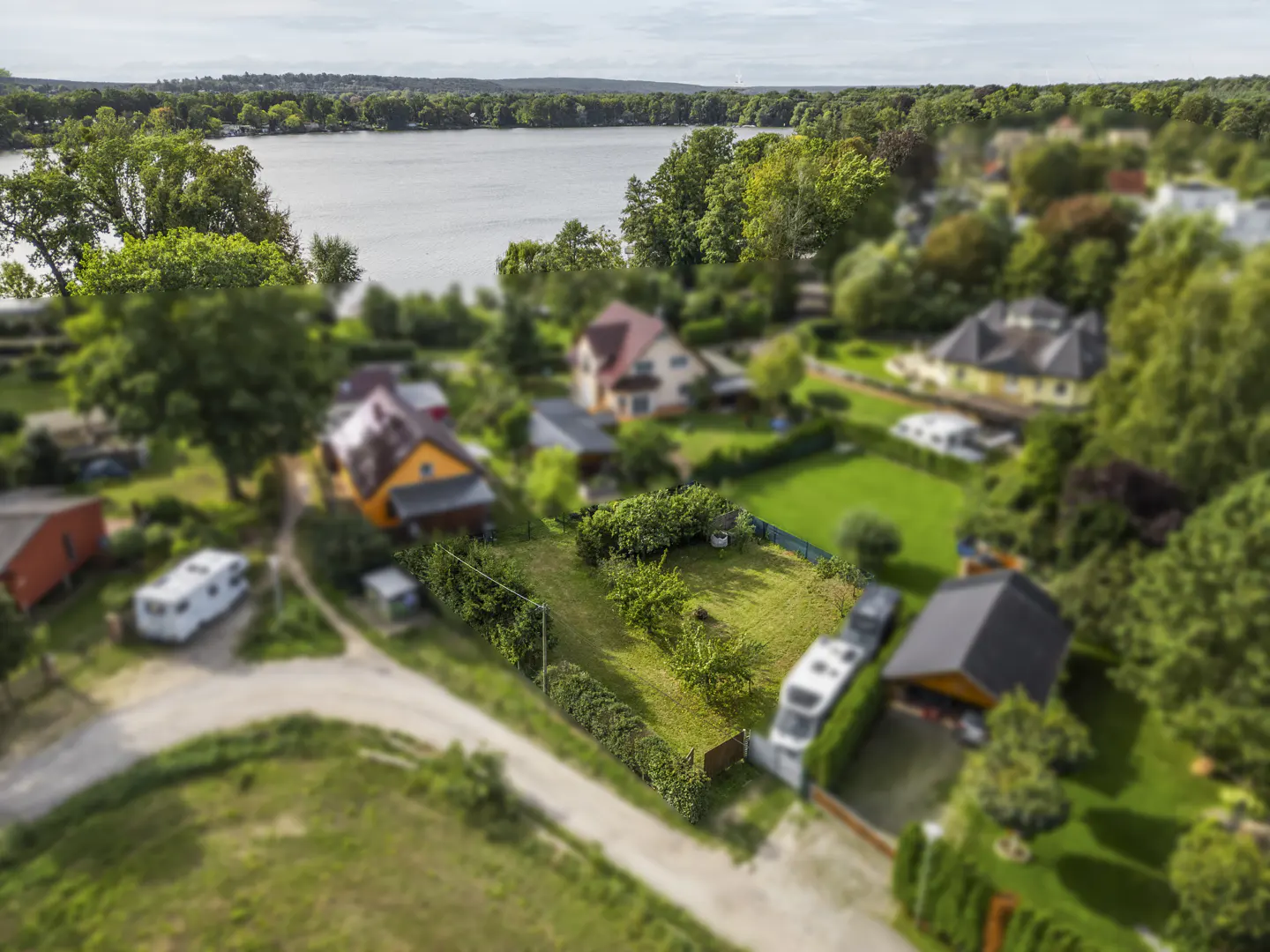 Aerial view of a green lot surrounded by houses, trees, and a lake in the background.