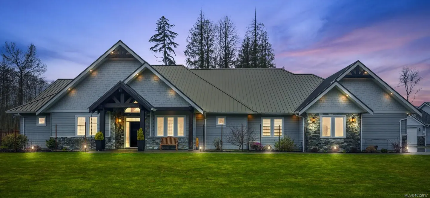 Exterior shot of a gray house with a metal roof, stone accents, and a green lawn at dusk.