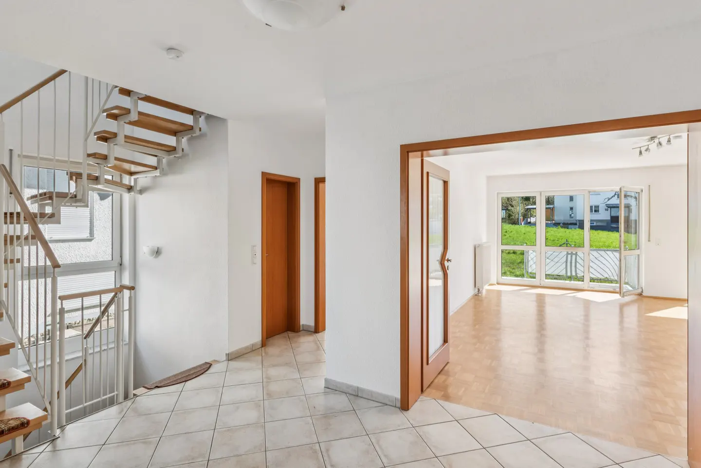 Bright foyer with a spiral staircase, tile floor, and open doorway to a living room with a large window.